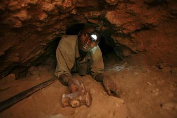 man wearing a black jacket, white shirt, blue jeans, and brown boots, playing a white electric guitar while sitting on an amp
