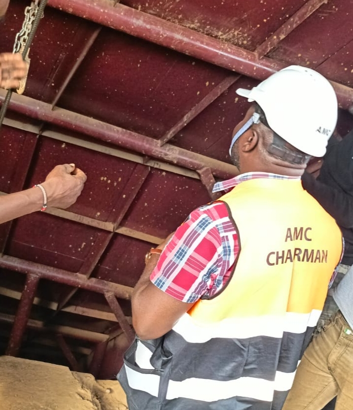 person writing in a notebook beside by an iPad, laptop, printed photos, spectacles, and a cup of coffee on a saucer