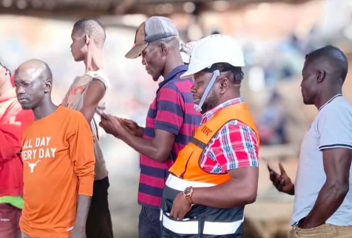 person writing in a notebook beside by an iPad, laptop, printed photos, spectacles, and a cup of coffee on a saucer