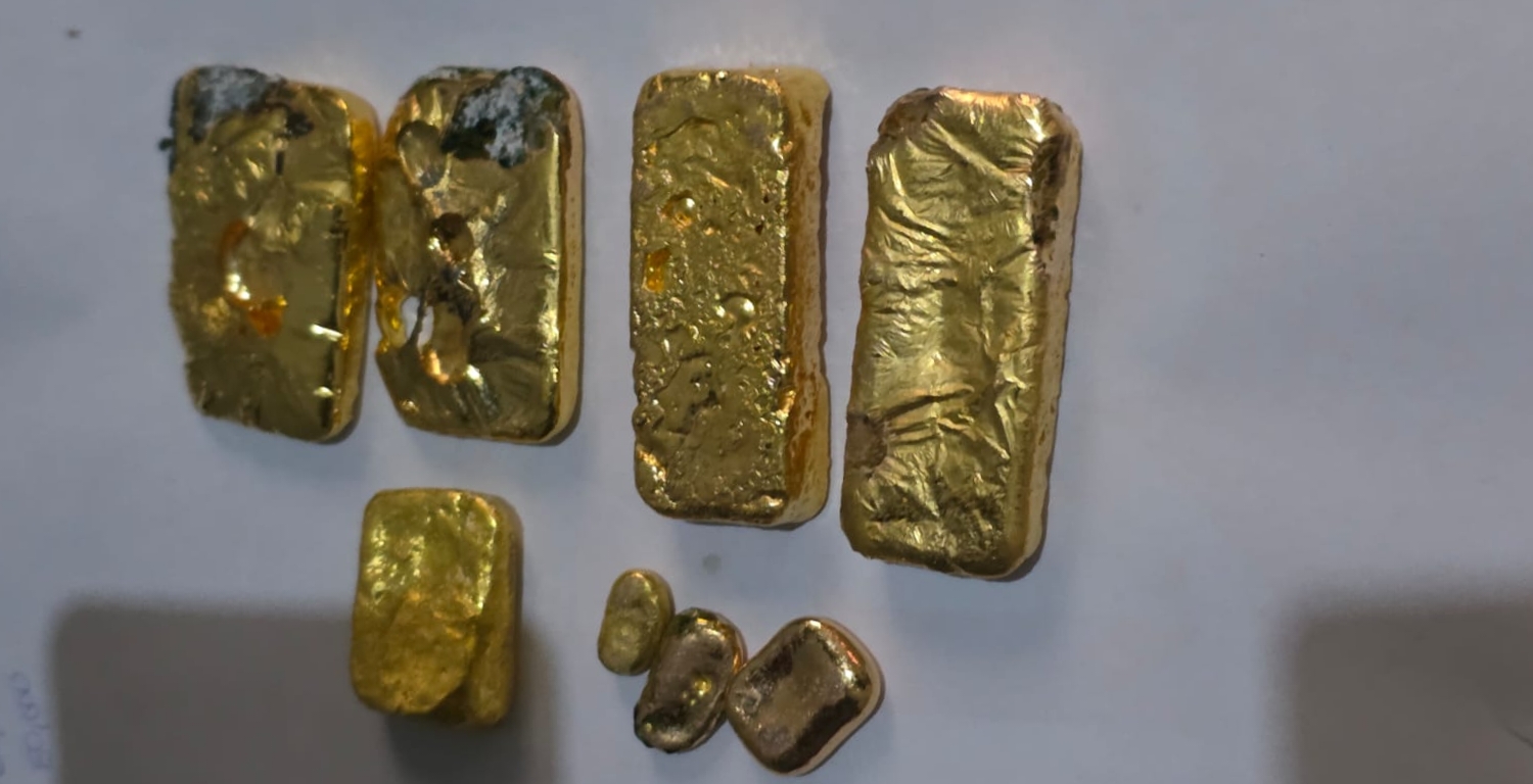 person writing in a notebook beside by an iPad, laptop, printed photos, spectacles, and a cup of coffee on a saucer